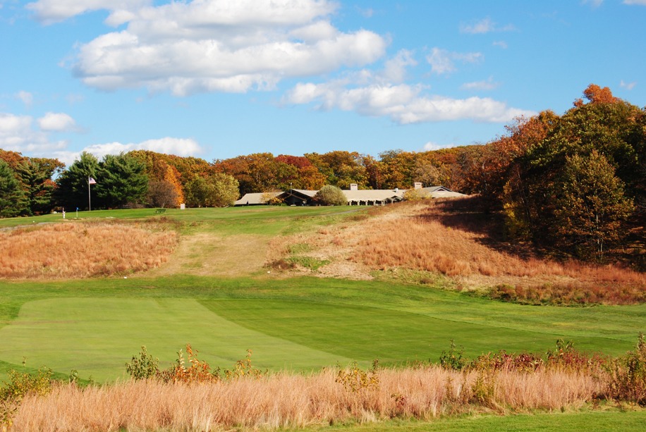 Tall grass lines the wide fairway going uphill to the elevated green.
