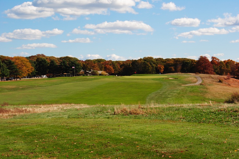Long, wide open fairway leading to a large green with dense wood coverage just beyond.