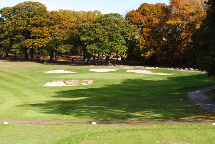 Shaded fairway leading to a sunny green with a sand trap up front and three more sand traps behind the green.